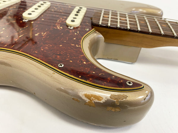 Close-up of a vintage electric guitar body showing worn gold finish and tortoiseshell pickguard with white single-coil pickups and chrome screws, featuring a maple neck with metal frets on a white background.