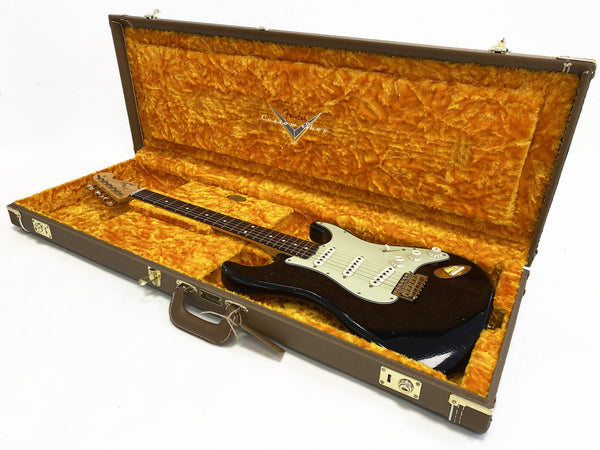 Vintage Fender Stratocaster electric guitar with black finish and white pickguard inside a brown Fender Custom Shop hard case lined with orange plush interior