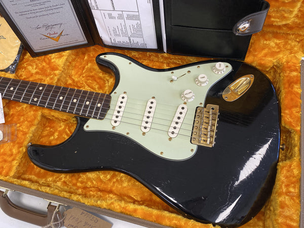 Close-up of black Fender Stratocaster electric guitar with white pickguard and three single-coil pickups in orange plush-lined hard case with Fender Custom Shop certificate and documents