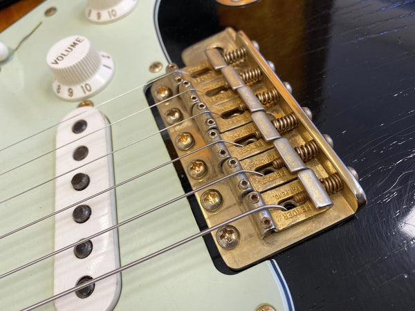Close-up of vintage Fender tremolo bridge and white single-coil pickup on electric guitar with volume knob set to 10