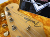 Close-up of Fender Stratocaster guitar headstock with tuning pegs and strings inside a yellow plush guitar case