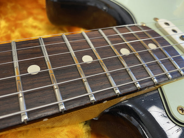 Close-up of electric guitar rosewood fretboard with dot inlays and metal frets on a sunburst body guitar resting on a yellow plush surface