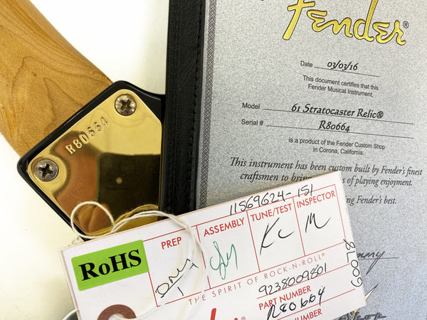 Close-up of Fender 61 Stratocaster Relic neck plate with serial number R80664, accompanying Fender certificate of authenticity dated 03/03/16, and RoHS compliance tag from Coffee House Guitars.