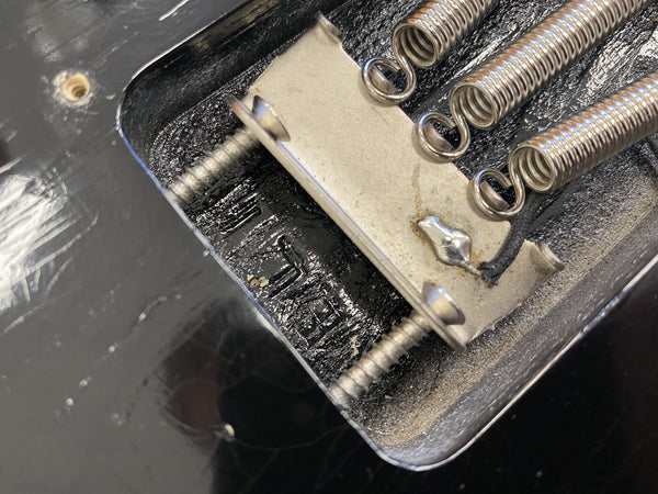 Close-up of guitar tremolo bridge springs and claw mounted on black electric guitar body, showing metal screws and vintage-style hardware components.