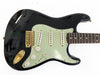 Black electric guitar with mint green pickguard, three single-coil pickups, volume and tone control knobs, and gold hardware on white background
