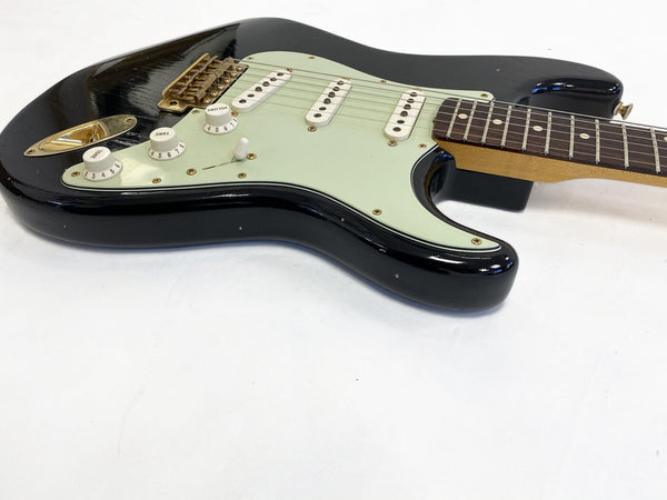 Black electric guitar with white pickguard, three single-coil pickups, volume and tone control knobs, and rosewood fingerboard on white background