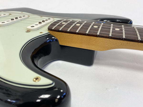 Close-up of black electric guitar body with white pickguard and maple neck with rosewood fretboard showing frets and strings