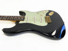 Black electric guitar with white pickguard, three single-coil pickups, and gold hardware on white background