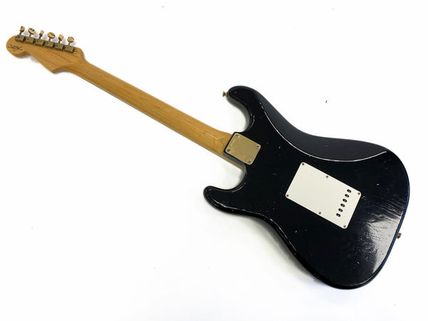 Black electric guitar with maple neck and vintage tuning pegs showing back view with cream plastic cover plate on white background