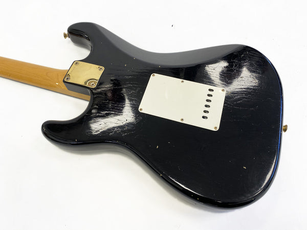 Black electric guitar body with white backplate and natural wood neck, showing wear and scratches on finish, photographed on white background