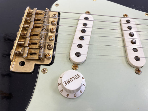 Close-up of vintage electric guitar bridge, two single-coil pickups, and white volume knob on light-colored guitar body