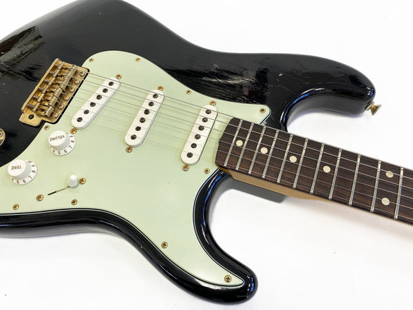 Black electric guitar with triple white single-coil pickups, white volume and tone knobs, and rosewood fretboard on white background