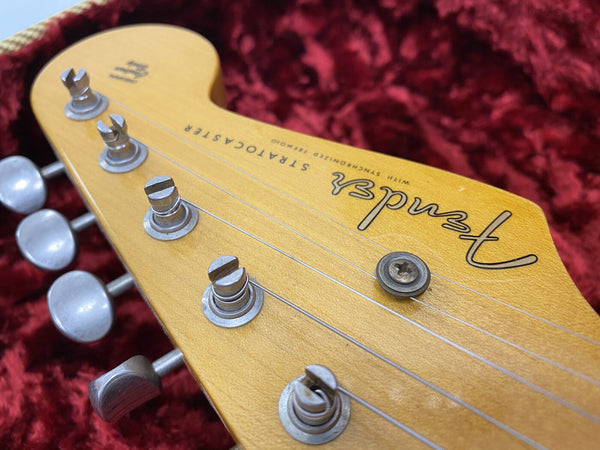 Close-up of Fender Stratocaster guitar headstock with tuning pegs and strings, natural wood finish on red velvet background