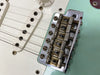 Close-up of vintage Fender electric guitar bridge and single-coil pickups on seafoam green body with white pickguard and volume knob.