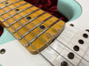 Close-up of aged maple guitar fretboard with visible wear and metal frets on a light blue electric guitar body with white pickguard and single coil pickups.