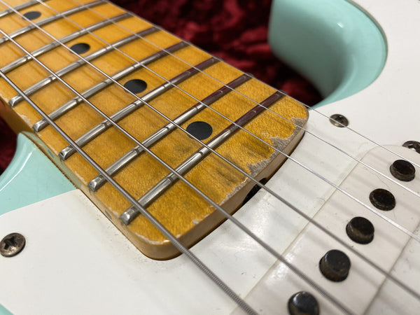 Close-up of aged maple guitar fretboard with visible wear and metal frets on a light blue electric guitar body with white pickguard and single coil pickups.