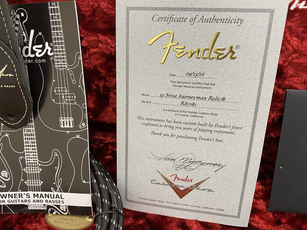 Fender Certificate of Authenticity for 55 Strat Journeyman Relic guitar with serial number R87781, accompanied by Fender owner's manual and guitar cable on red plush background.