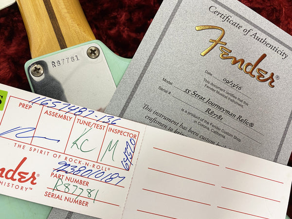 Close-up of Fender Custom Shop certificate of authenticity and assembly card for a 55 Strat Journeyman Relic electric guitar with serial number R87781 and signed inspection details.