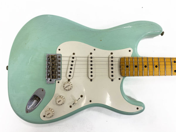 Seafoam green electric guitar with white pickguard and maple fretboard, vintage-style single-coil pickups and tone control knobs, close-up view on white background
