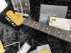 Close-up of Fender Stratocaster guitar headstock and fretboard with owner's manual, Fender Custom Shop certificate, guitar pick, and accessories in soft guitar case interior