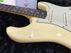 Close-up of vintage cream Fender Stratocaster electric guitar body and rosewood fretboard showing aging and wear with Fender certificate in background on black plush surface