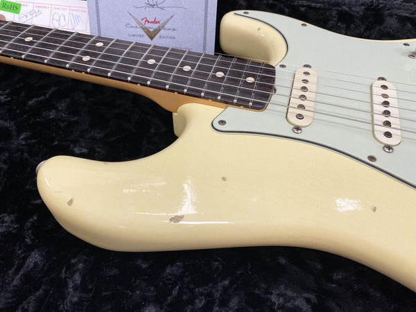 Close-up of vintage cream Fender Stratocaster electric guitar body and rosewood fretboard showing aging and wear with Fender certificate in background on black plush surface