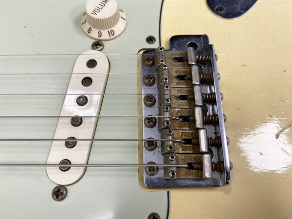 Close-up of vintage Fender Stratocaster electric guitar bridge, single coil pickup, volume knob, and strings on aged cream finish body.