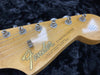 Close-up of Fender Stratocaster guitar headstock with tuning pegs and string tree on natural wood finish against black background