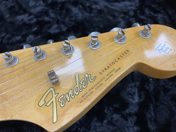Close-up of Fender Stratocaster guitar headstock with tuning pegs and string tree on natural wood finish against black background