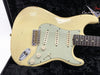 Vintage cream Fender Stratocaster electric guitar with three single-coil pickups and mint green pickguard showing natural wear and aging in black guitar case
