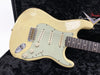 Vintage cream Fender Stratocaster electric guitar with aged wear and three single-coil pickups on black plush case interior