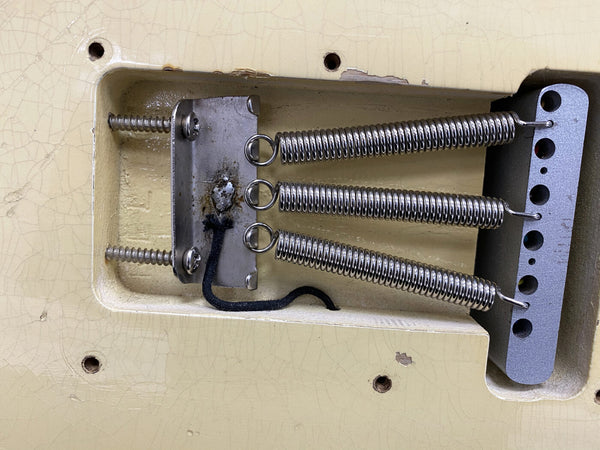 Close-up of vintage electric guitar tremolo cavity showing three metal tension springs and claw mounted on aged cream body wood with cracks and chip paint