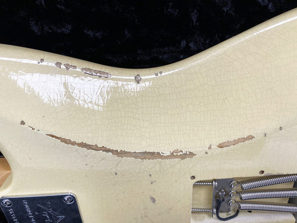 Close-up of cream-colored electric guitar body showing vintage-style relic paint wear and checking near the spring cavity and neck plate with visible metal springs and screws.