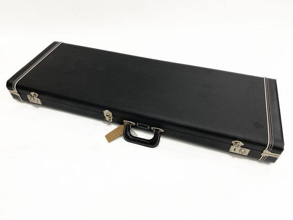 Black rectangular guitar hard case with silver metal latches and handle, white stitching detail, and a small brown tag attached to the handle.