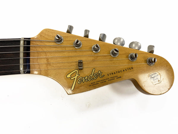 Fender Stratocaster guitar headstock with tuning pegs and strings, natural wood finish, original decal sticker, close-up view.