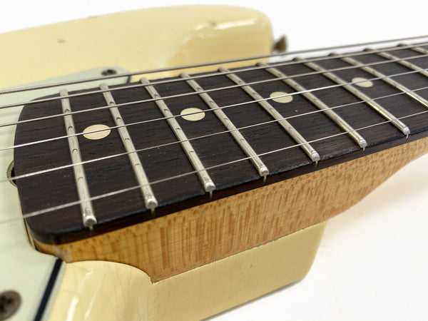 Close-up of electric guitar fretboard with dot inlays, metal frets, and cream-colored body edge showing wood grain finish