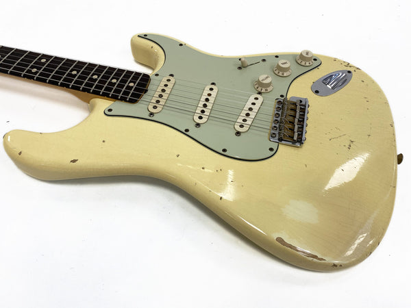 Close-up of vintage cream electric guitar body with three single-coil pickups, mint green pickguard, and aged finish showing wear and relic details on white background