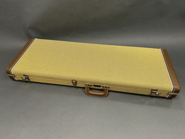 Closed vintage style guitar case with tan tweed fabric and brown leather corners and handle on gray background