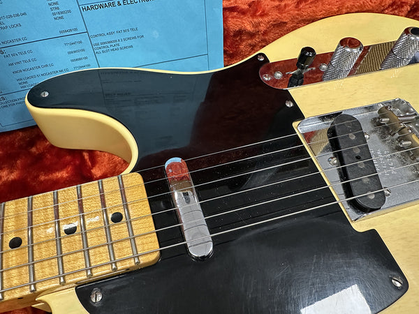 Close-up of vintage-style Telecaster electric guitar with cream body, black pickguard, maple neck, and chrome hardware on orange plush background with blue hardware and electronics note.