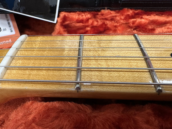 Close-up of electric guitar maple fretboard with metal frets and steel strings on orange plush case lining