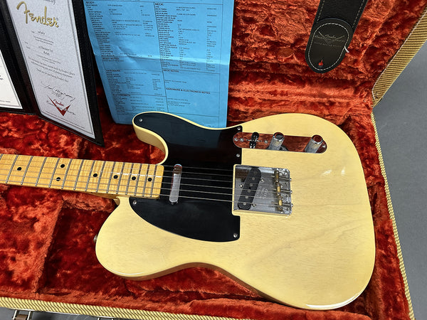 Fender Telecaster electric guitar with maple neck and vintage blonde finish resting in a reddish-orange plush lined hardshell case, accompanied by Fender certificate and specification sheet.