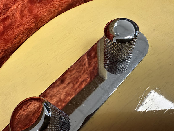 Close-up of chrome control knobs on vintage cream electric guitar body with reflective surface and textured metal finish