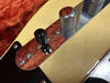 Close-up of vintage cream electric guitar control plate with chrome knob and black toggle switch on reddish background