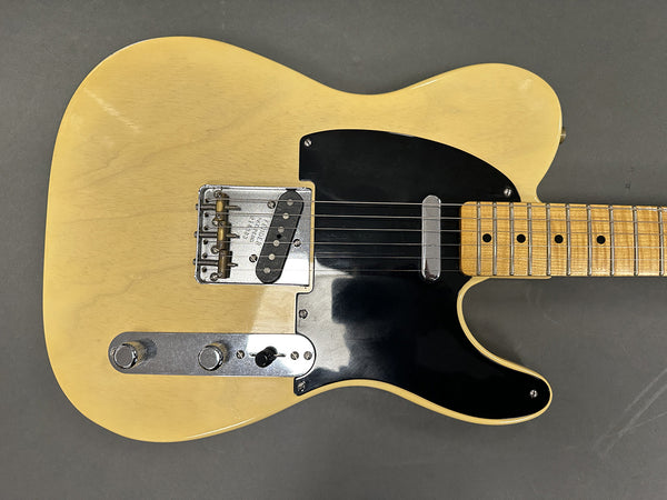 Vintage blond solid body electric guitar with black pickguard and maple neck, close-up of strings and bridge on grey background