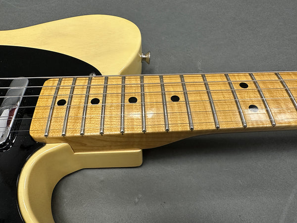Close-up of maple neck and fretboard on vintage cream electric guitar with black pickguard and metal bridge plate on gray background