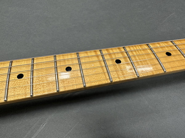 Close-up of figured maple guitar neck and fretboard with metal frets and black dot inlays against a gray background
