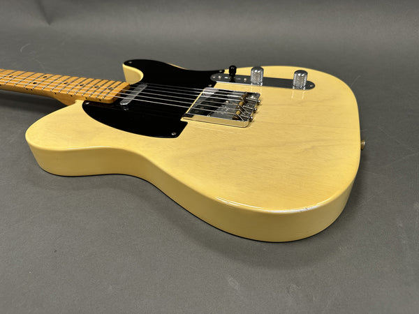Close-up of cream-colored electric guitar body with black pickguard, chrome bridge, and control knobs on gray background