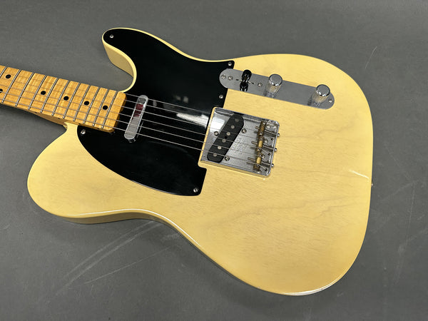 Close-up of cream electric guitar body with black pickguard, maple neck, and chrome control knobs and bridge on gray background