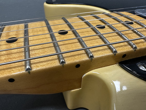 Close-up of maple guitar neck with steel frets and black dot inlays on a cream electric guitar body