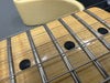 Close-up of electric guitar maple fretboard with metal frets and black dot inlays, steel strings, and cream-colored guitar body edge.